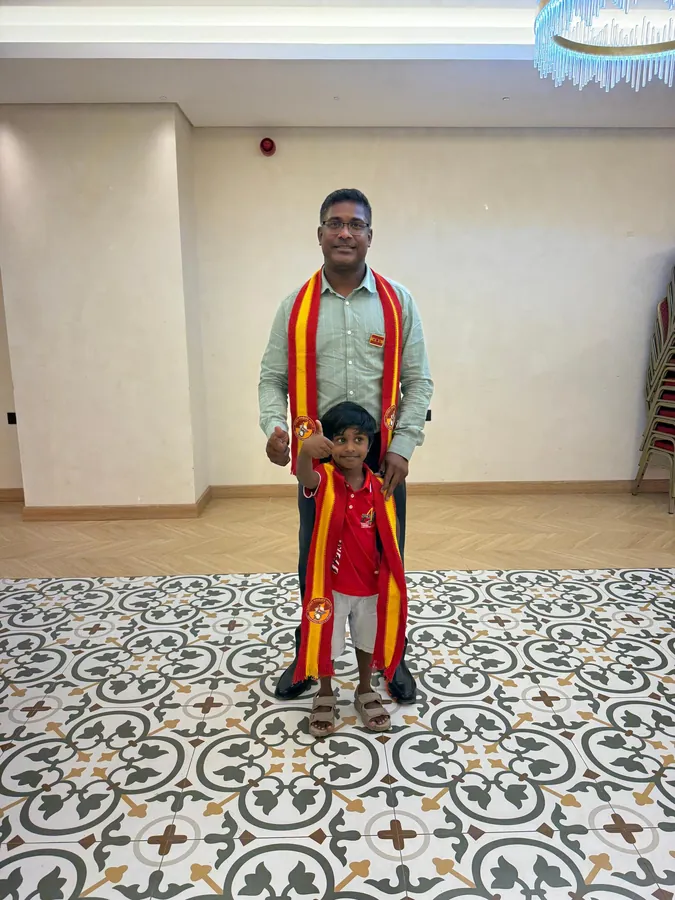 கழக மேலாடை அணிந்த உறுப்பினரும் அவரது மகனும் மண்டபத்தில் நிற்கும் புகைப்படம்.